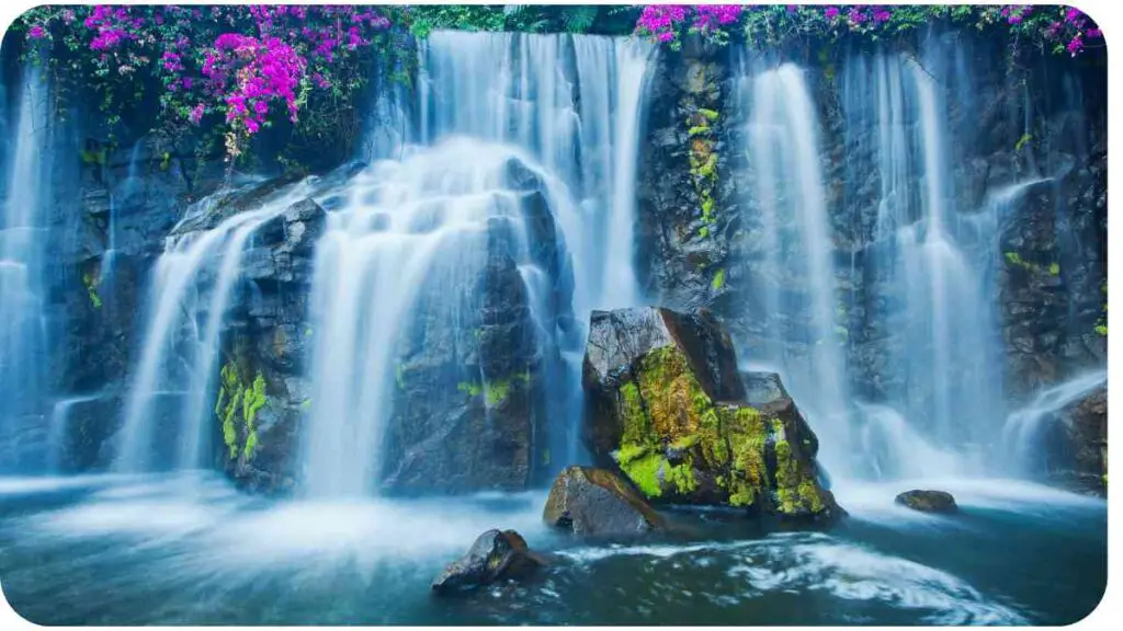 a waterfall with purple flowers in front of it